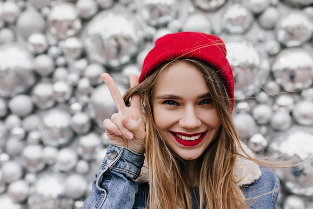 Foto gratuita primer plano de mujer caucásica soñadora en chaqueta de mezclilla posando con placer retrato de niña romántica con cabello castaño claro riendo sobre fondo brillante con bolas de discoteca