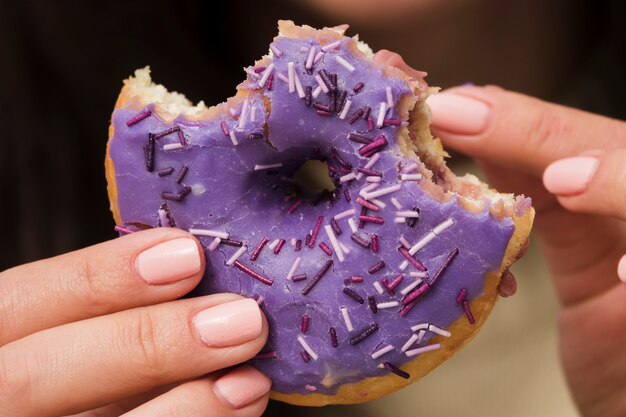 Primer plano de una mujer comiendo donut púrpura