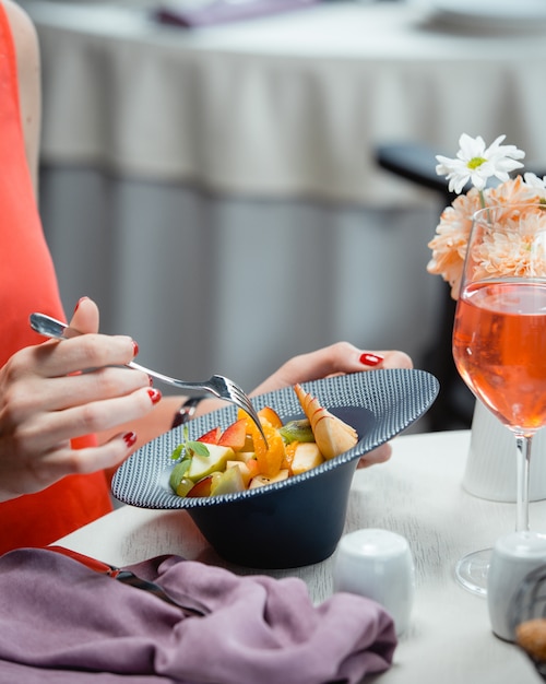 Un primer plano de mujer comiendo ensalada de frutas con manzana, naranja, kiwi