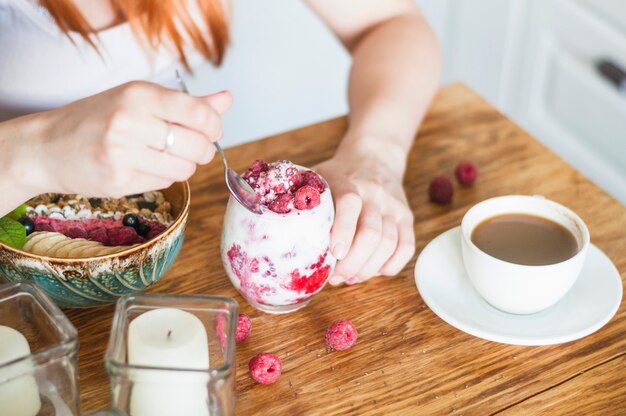 Primer plano de mujer comiendo yogurt con frambuesa en mesa de madera