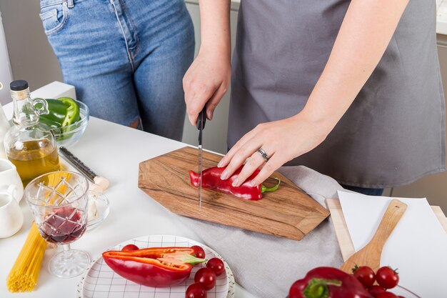 Primer plano de mujer cortando el pimiento rojo con un cuchillo en una tabla de cortar sobre el escritorio