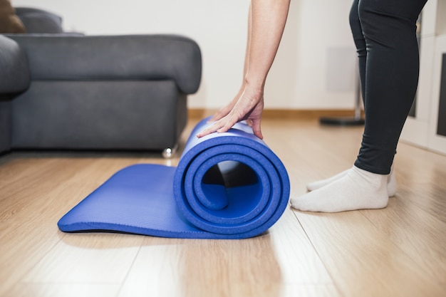 Primer plano de una mujer doblando un mate de yoga azul después de hacer ejercicio en casa