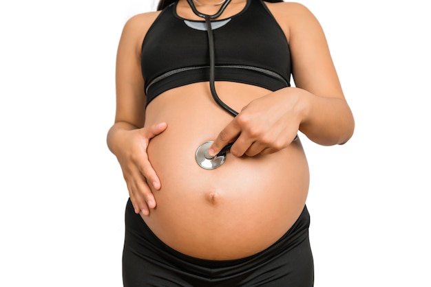 Primer plano de la mujer embarazada con estetoscopio en el vientre escuchando al bebé
