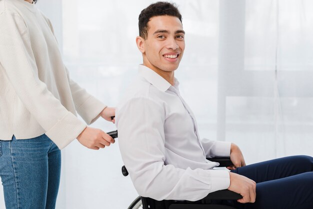 Primer plano de una mujer empujando al joven sonriente sentado en silla de ruedas