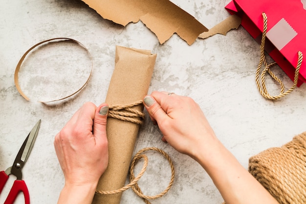 Primer plano de una mujer envolviendo la caja de regalo con una cuerda de yute sobre fondo texturizado