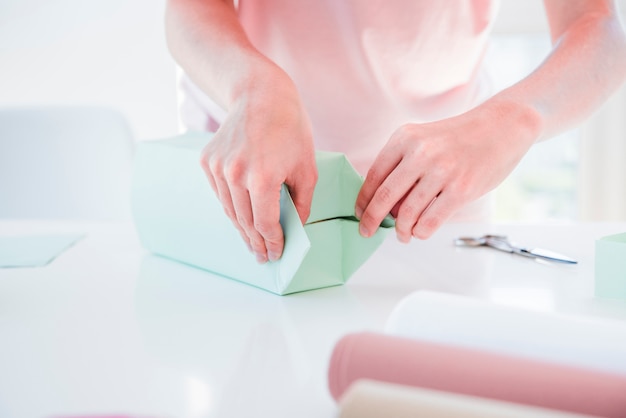 Primer plano de una mujer envolviendo la caja de regalo en mesa blanca