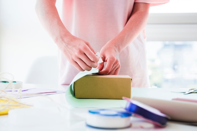 Foto gratuita primer plano de una mujer envolviendo la caja de regalo en la mesa