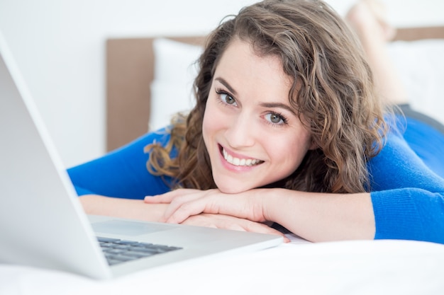 Primer plano de la mujer feliz trabajando en la computadora portátil en la cama