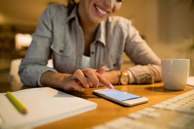 Primer plano de mujer feliz usando teléfono móvil y mensajes de texto por la noche en casa