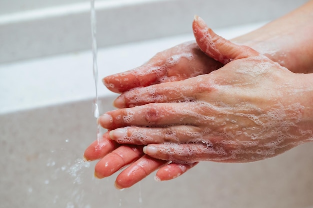 Primer plano de una mujer frotándose las manos con un jabón en el baño.