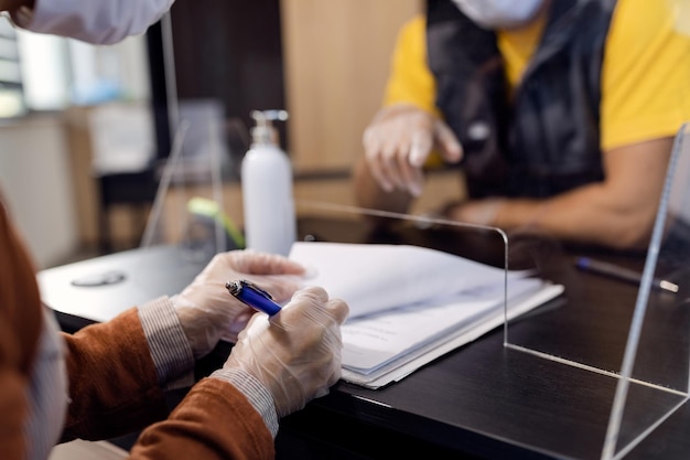 Primer plano de una mujer con guantes protectores mientras firma documentos en la oficina del taller de automóviles