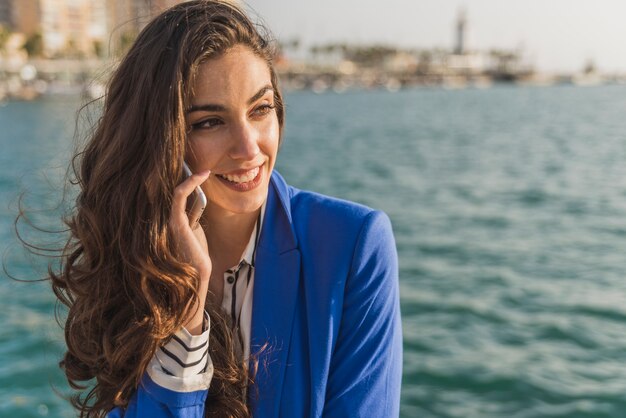 Primer plano de mujer guapa hablando por teléfono con el mar de fondo