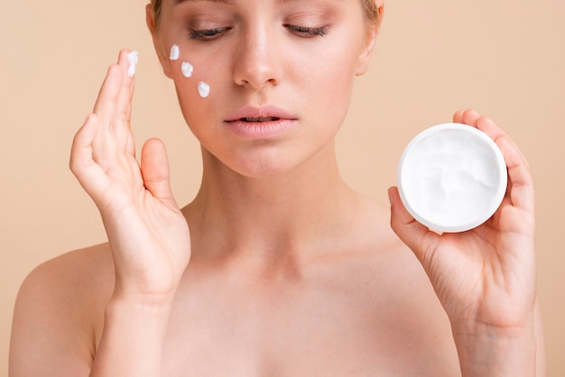 Primer plano mujer hermosa con crema para la cara y tarro