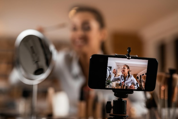 Primer plano de una mujer influyente que aplica productos de belleza mientras filma un vlog de maquillaje