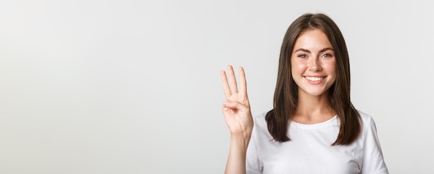 Foto gratuita primer plano de una mujer joven atractiva alegre sonriendo mostrando tres dedos fondo blanco.