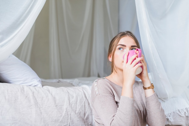 Primer plano de mujer joven bebiendo café sentado cerca de la cama