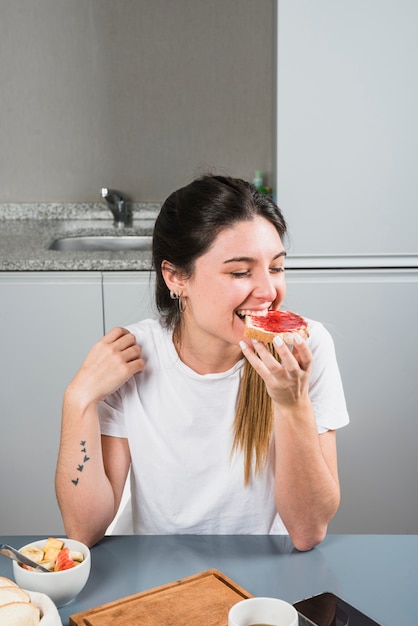 Primer plano de una mujer joven comiendo mermelada con pan en el desayuno