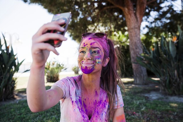 Primer plano de una mujer joven cubierta con holi color tomando selfie en teléfono móvil