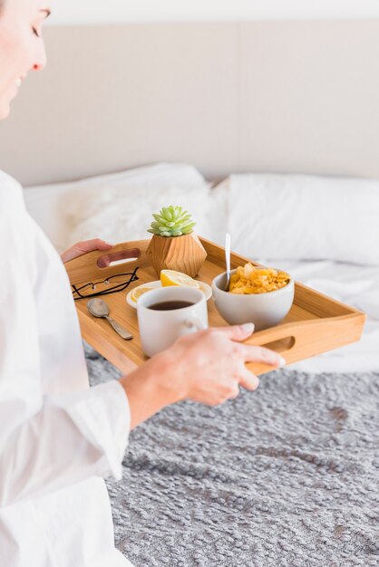 Primer plano de mujer joven con desayuno por la mañana en la bandeja de madera