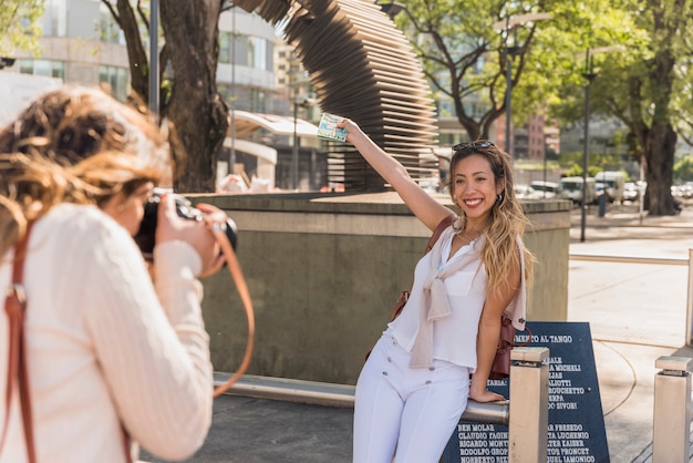 Primer plano de mujer joven fotografiando a su amiga elevando sus brazos mostrando mapa