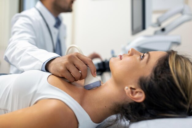 Primer plano de una mujer joven que le examina el cuello con un médico usando un escáner de ultrasonido en una clínica moderna