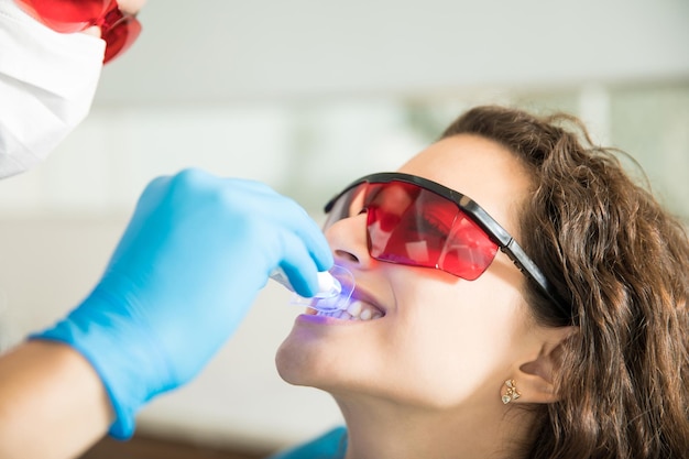 Primer plano de una mujer joven que tiene sus dientes blanqueados con luz ultravioleta en una clínica dental