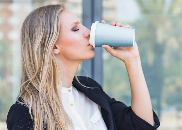 Primer plano de mujer joven rubia bebiendo para llevar café