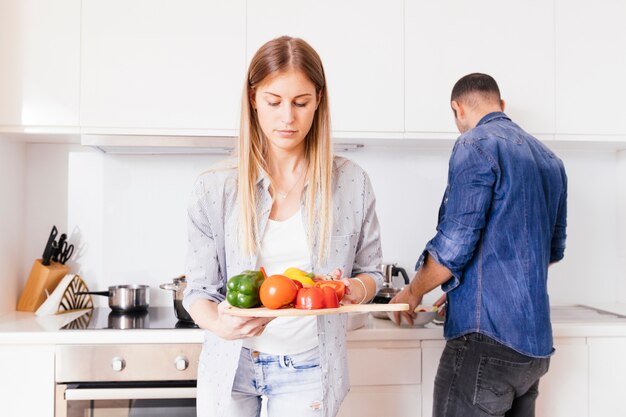 Primer plano de mujer joven rubia con coloridos pimientos en la mano con su marido en el fondo