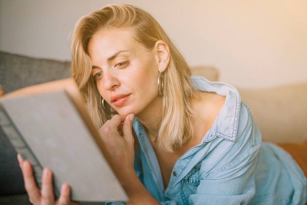 Foto gratuita primer plano de mujer joven rubia con la mano en la barbilla leyendo el libro