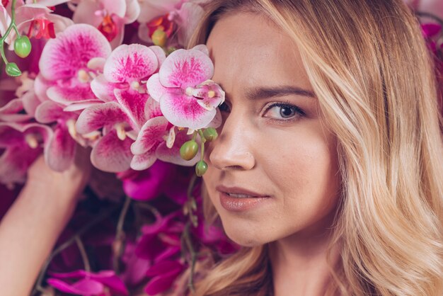 Primer plano de mujer joven rubia que cubre sus ojos con una orquídea rosa