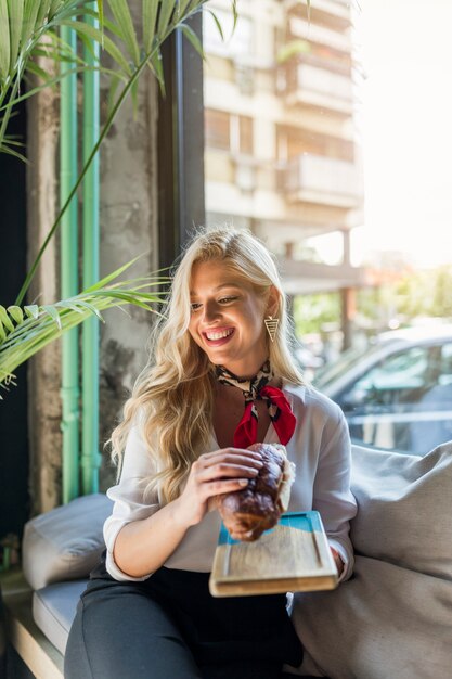 Primer plano de mujer joven rubia sentada en la cafetería con bandeja y pan