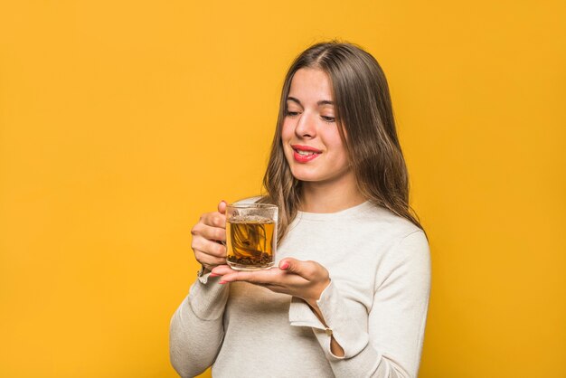 Primer plano de mujer joven sonriente mirando té de hierbas en la taza de vidrio