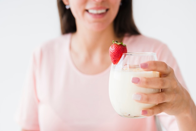 Primer plano de una mujer joven sonriente con vaso de yogur con fresa