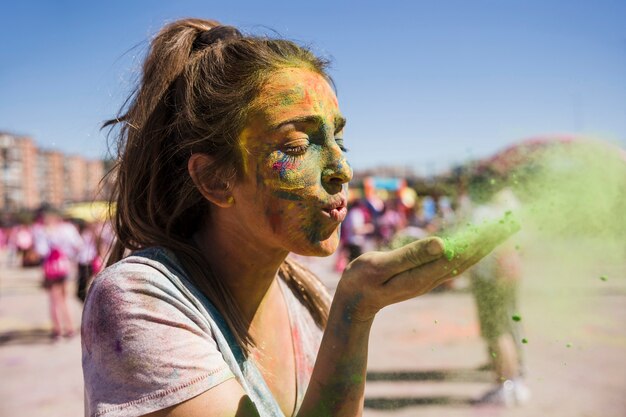 Primer plano de una mujer joven soplando color holi