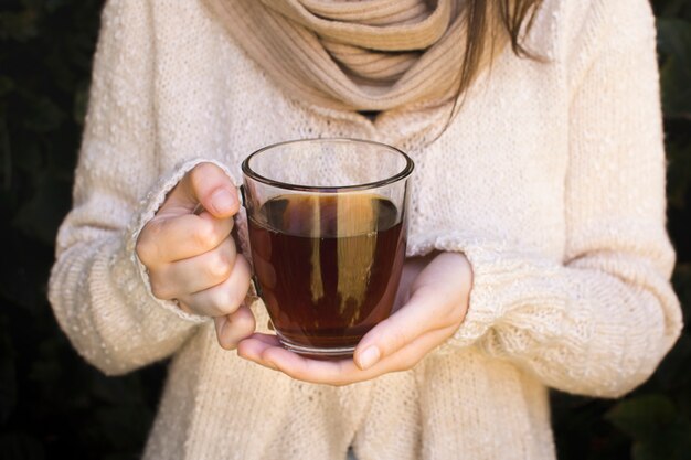 Primer plano de una mujer joven sosteniendo una taza transparente de té de hierbas