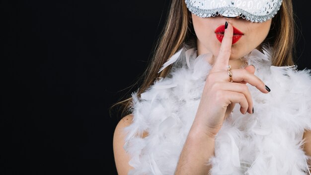 Primer plano de una mujer con máscara de carnaval con el dedo en sus labios