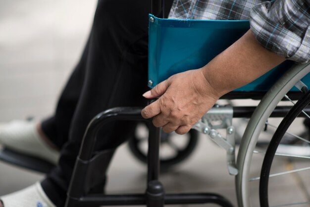 Primer plano, de, mujer mayor, mano, en, rueda, de, sillón de ruedas, durante, caminata, en, hospital