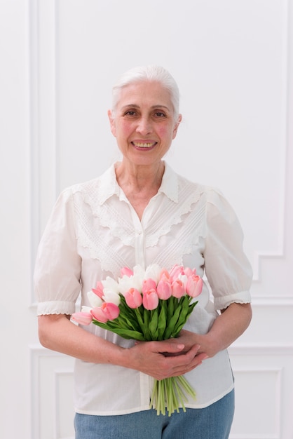 Primer plano de una mujer mayor con ramo de flores de tulipán mirando a cámara