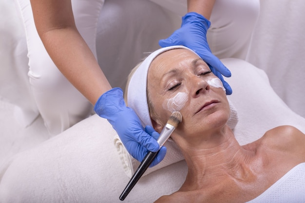 Primer plano de una mujer mayor de raza caucásica aplicar crema facial en un salón de belleza