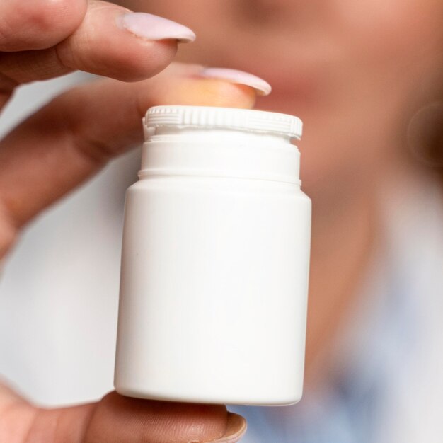 Primer plano de mujer médico desenfocado sosteniendo una botella de medicina