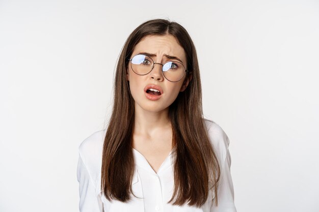 Primer plano de una mujer morena confundida con gafas que parece perpleja y despistada de pie sobre la espalda blanca...