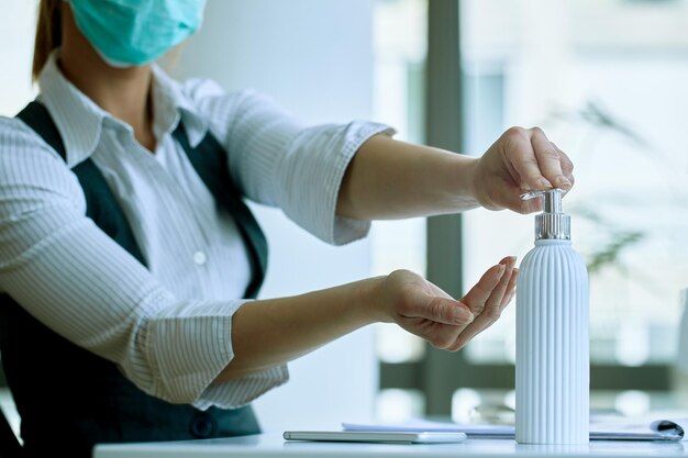 Primer plano de una mujer de negocios limpiándose las manos con gel antiséptico para manos en la oficina