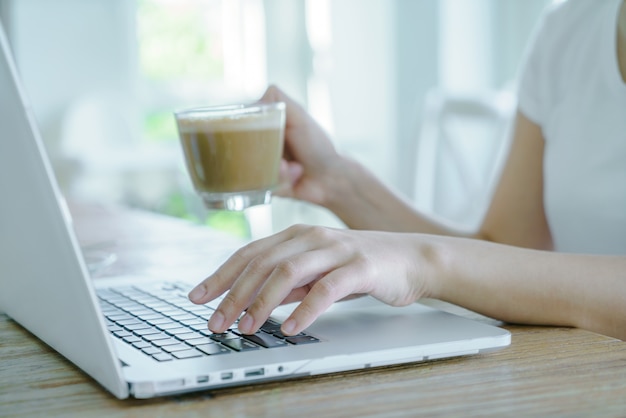 Primer plano de mujer de negocios de la mano escribiendo en el teclado del ordenador portátil y cof