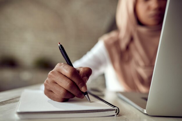Primer plano de una mujer de negocios musulmana negra escribiendo notas mientras trabaja en una computadora en la oficina