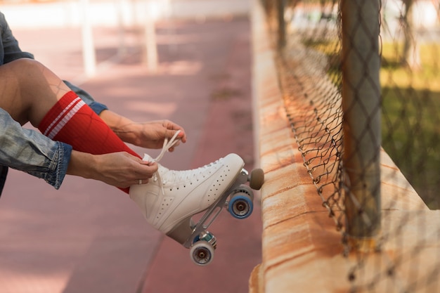 Primer plano de mujer patinadora inclinando su pie en la valla atar encaje