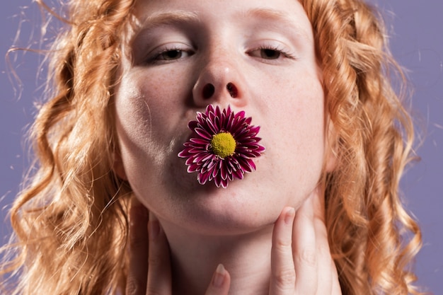 Primer plano de mujer pelirroja posando con un crisantemo en la boca