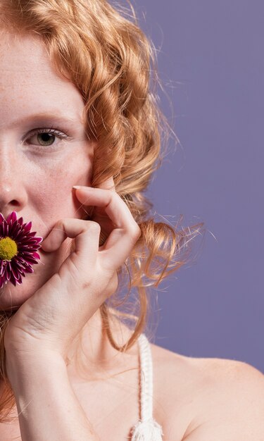 Primer plano de mujer pelirroja posando con una flor en la boca