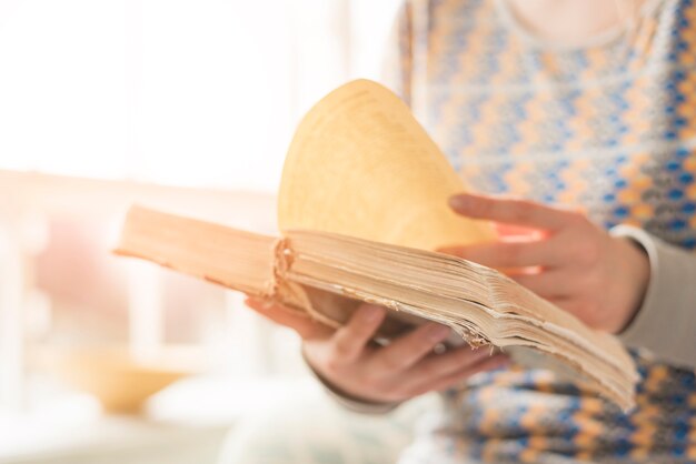 Primer plano de una mujer de pie cerca de la ventana girando la página del libro