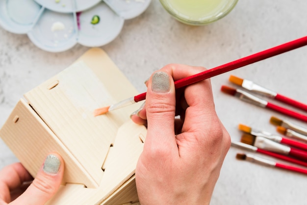 Primer plano de mujer pintando el modelo de casa de madera con pincel