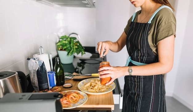 Primer plano de mujer poniendo salsa en la pasta cocida en el plato